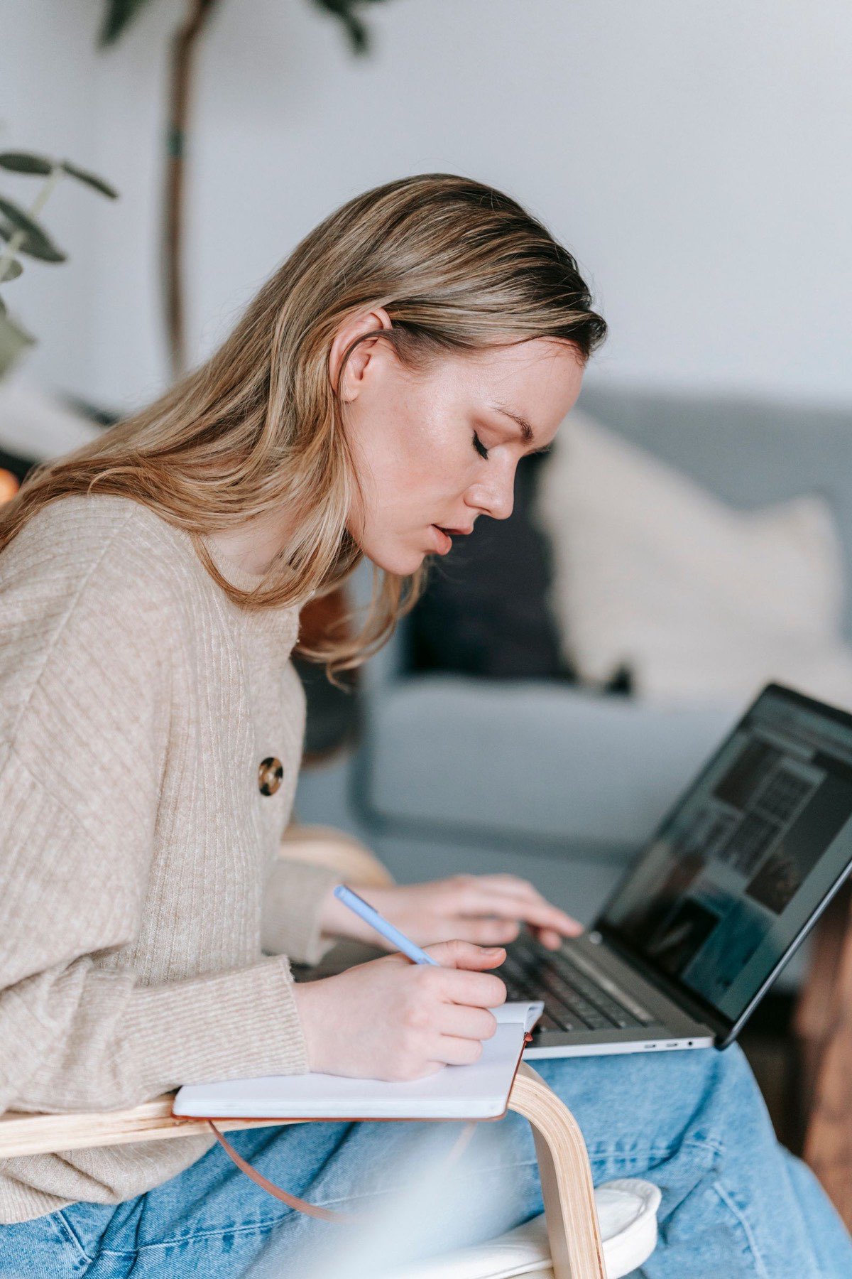 A student writing notes in a planner while working on a laptop